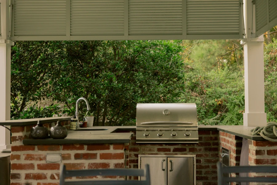 An outdoor kitchen with a grill and chairs